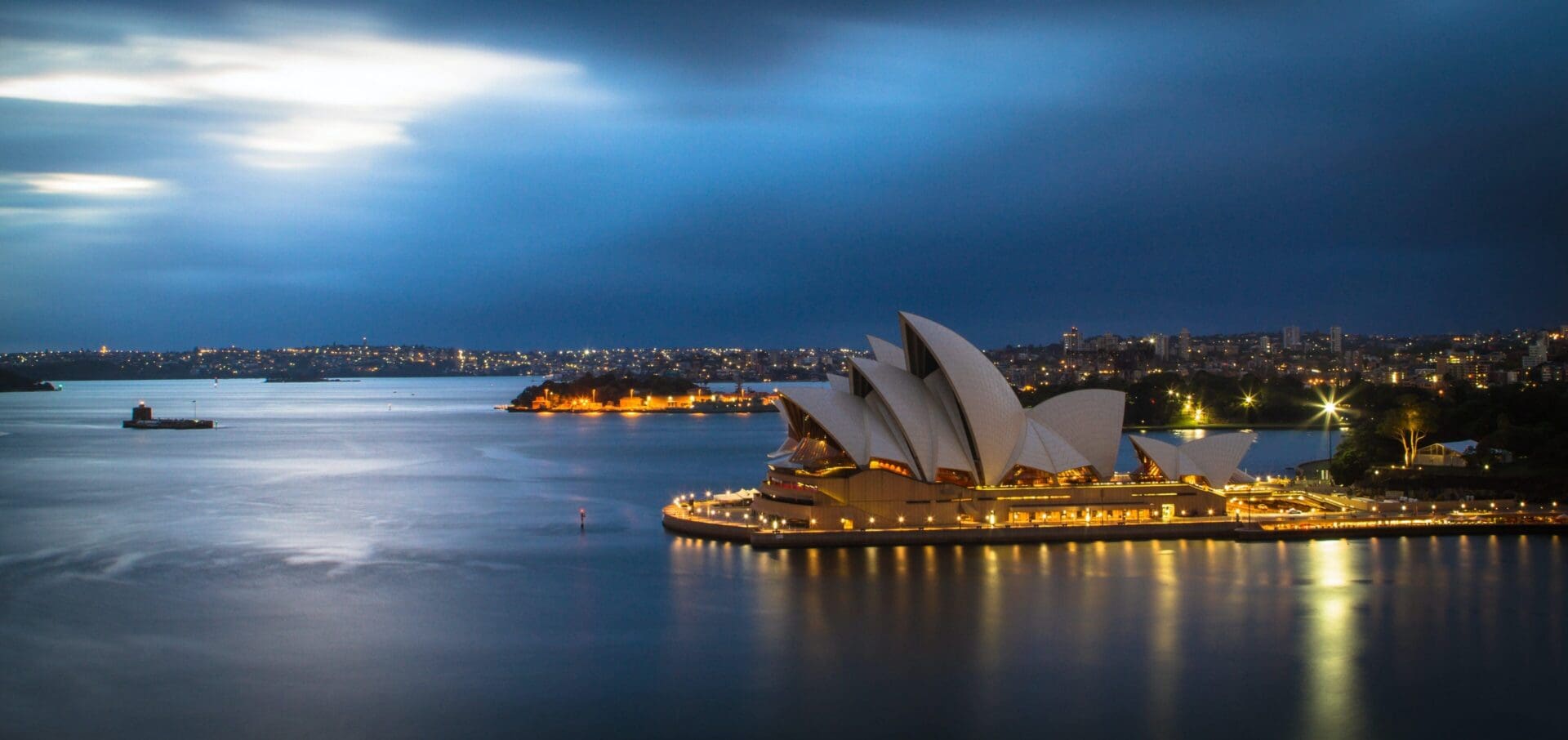 Sydney Opera House illuminated at night, waterfront view.