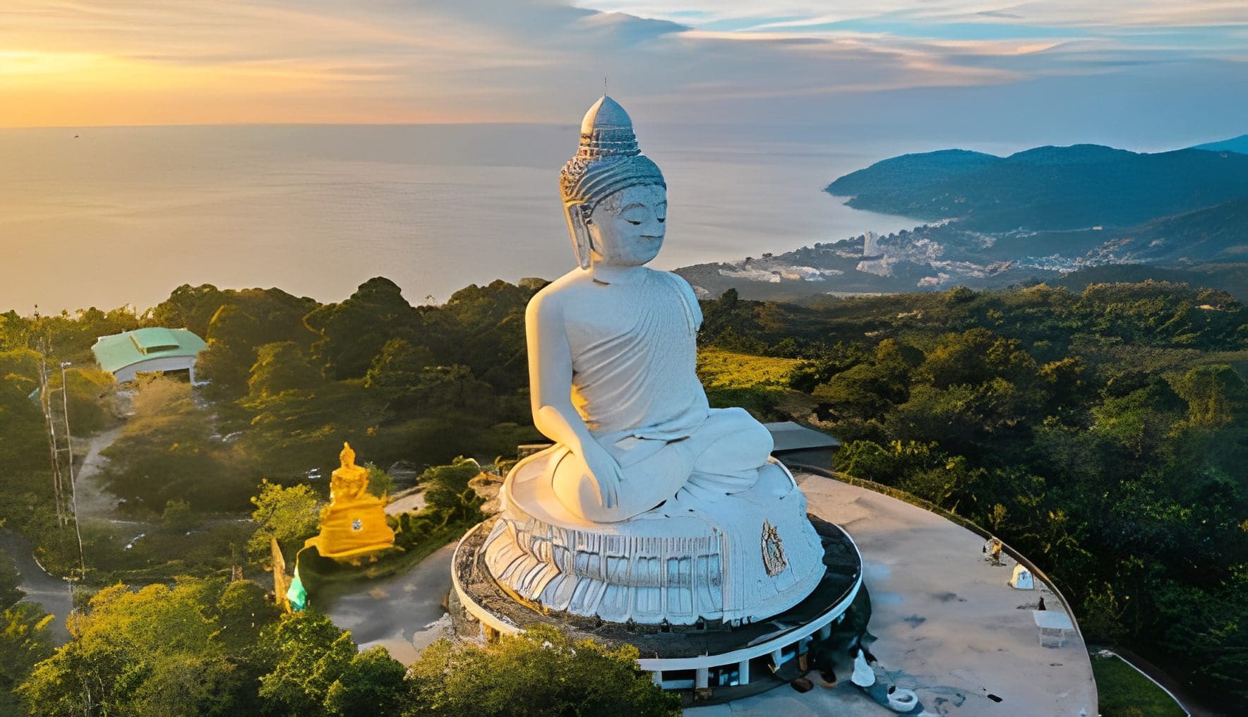 Giant Buddha statue overlooking lush hills and sea.