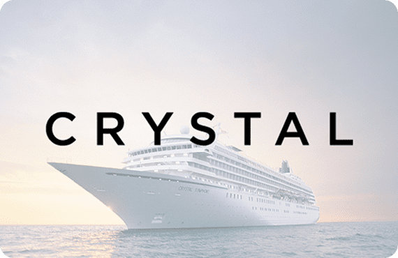 A large white cruise ship named Crystal sails on calm waters during sunrise or sunset.
