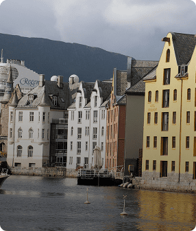 Colorful buildings along a waterfront, mountains behind.