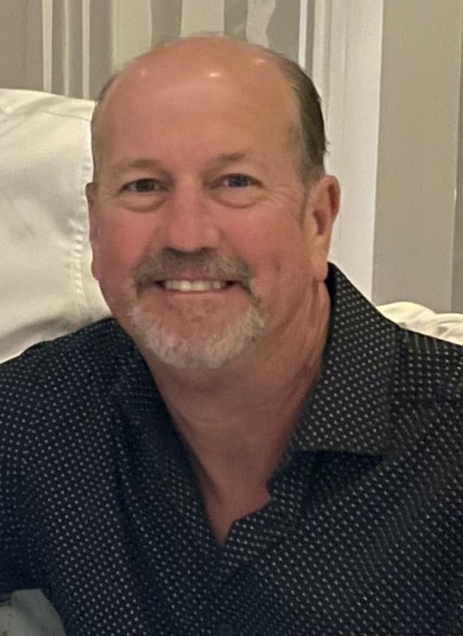 Smiling man wearing a black dotted shirt.